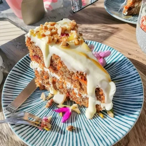 Saftiger Karottenkuchen mit cremigem Frischkäse-Frosting auf einem weißen Teller.