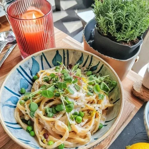 Pasta al Limone mit frischen Erbsen auf einem Teller garniert mit Zitronenmelisse
