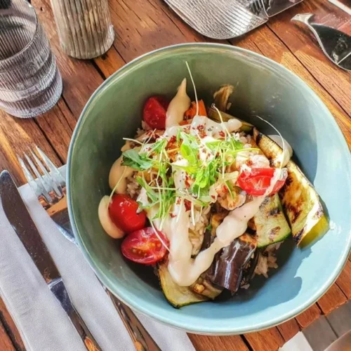 Reisbowl mit gegrilltem Gemüse und Tahini-Sauce auf einem Teller